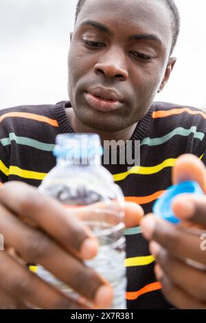 Schwarzer Mann im farbenfrohen Pullover, der eine Flasche Wasser hält, was auf Hypoglykämie-Symptome hinweist Stockfoto