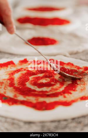 Ein anonymer Koch in einer Pizzeria verteilt Tomatensauce auf Pizzateig mit einer Kelle Stockfoto