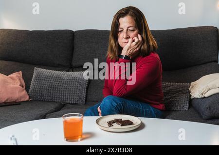 Eine Frau sitzt auf einer Couch und sieht verstört aus, möglicherweise leidet sie an hypoglykämischen Symptomen mit einem Teller mit Essen und einem Getränk, das unberührt auf dem Tisch liegt Stockfoto