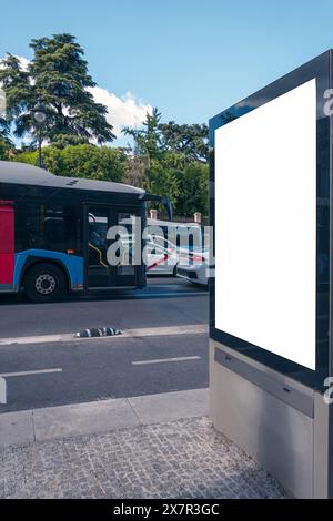 Eine leere Plakatwand steht bereit für Ihre Werbung auf einer belebten Straße in Madrid, mit vorbeifahrenden Bussen und Autos vor der Kulisse üppiger Bäume Stockfoto