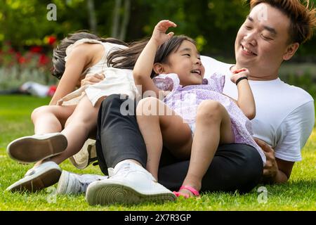 Eine asiatische Familie lacht zusammen während eines Urlaubs in einem üppigen europäischen Park und schafft glückliche Erinnerungen Stockfoto