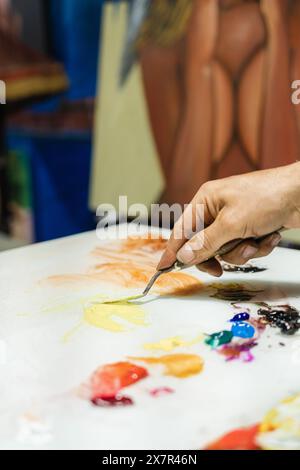 Zugeschnittener, nicht erkennbarer Mann, der während einer kreativen Studiosession Farbe auf einer Palette mit Präzision mischt, Pinsel in der Hand. Stockfoto
