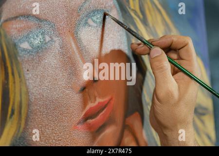 Der zugeschnittene, nicht erkennbare Mann malt akribisch feine Details auf eine Leinwand und fokussiert sich dabei auf den Gesichtsausdruck ihres Motivs in einem Kunststudio. Stockfoto