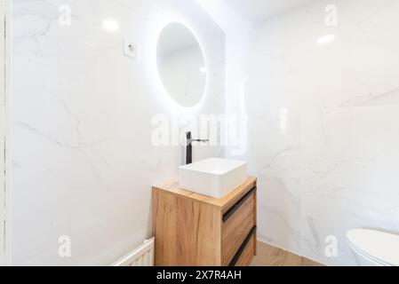 Dieses Bild zeigt ein stilvolles, unbewohntes Apartment-Badezimmer mit einer eleganten weißen Marmorwand und einem trendigen rechteckigen Waschbecken auf einer hölzernen Vanit Stockfoto