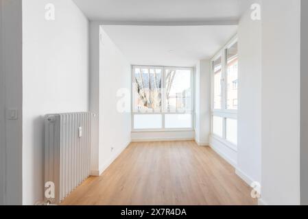 Dieses Bild zeigt ein helles und luftiges, leeres Apartmentinnere, das sich auf einen gut beleuchteten Raum mit großen Fenstern, Holzböden und makellos weißen Wänden konzentriert Stockfoto