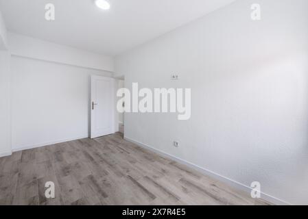 Ein minimalistisches Innenbild eines leeren städtischen Apartments mit makellos weißen Wänden, Holzfußboden und einer einzigen weißen Tür. Ideal für echte Estate Stockfoto