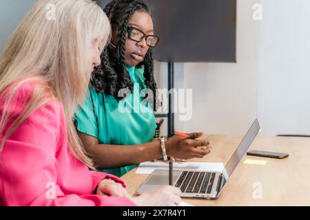 Zwei professionelle Frauen beteiligen sich an einem Gemeinschaftsprojekt in einem Coworking Space, das Teamwork und Vielfalt veranschaulicht Stockfoto