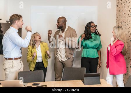 Eine vielfältige Gruppe von Fachleuten feiert freudig einen Sieg in ihrem Coworking-Büro mit motivierenden Gesten Stockfoto