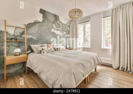 Ein modernes, luftiges Schlafzimmer mit einzigartiger künstlerischer Wandmalerei, Holzmöbeln und natürlichem Licht, das durch große Fenster strömt, kombiniert das Zimmer c Stockfoto