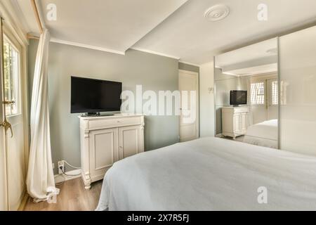Modernes, aber einladendes Schlafzimmer mit großem Bett, Flachbildfernseher und Tageslicht Stockfoto