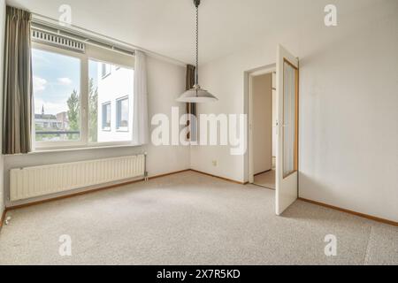 Geräumiger und hell beleuchteter leerer Raum mit großem Fenster, offener Tür und Hängeleuchte Stockfoto