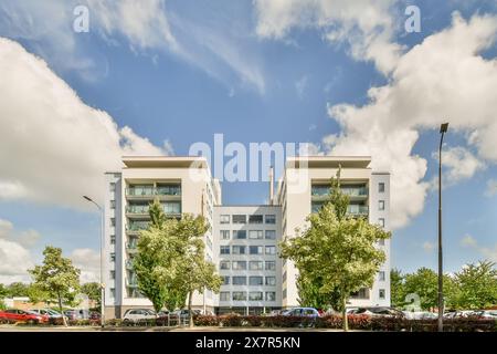 Moderne, architektonische, weiße Doppelhaushäuser, die sich unter einem klaren blauen Himmel mit üppigen grünen Bäumen im Vordergrund erheben Stockfoto
