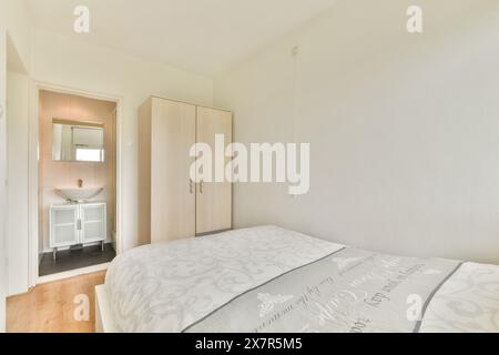 Helles, minimalistisches Schlafzimmer mit großem Bett, Holzschrank und offener Tür zum eigenen Bad. Stockfoto