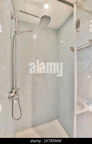 Moderne Dusche mit eleganten Armaturen und blauen Mosaikfliesen, Regendusche und Glastür. Stockfoto