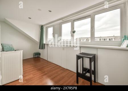 Ein einladender Dachboden mit Laminatboden aus Holz, einer schrägen Decke und drei Fenstern, die viel Tageslicht einlassen. Stockfoto