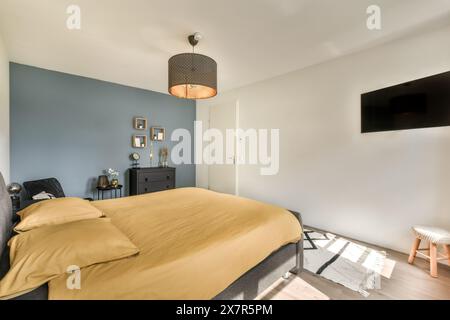 Modernes Schlafzimmer mit komfortablem Doppelbett, stilvoller Einrichtung und wandmontiertem Fernseher. Sauberes und gemütliches Design in Madrids Stadtappartement Stockfoto