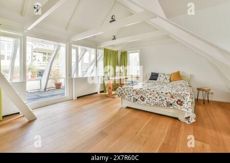 Ein wunderschön beleuchtetes Schlafzimmer im Dachgeschoss mit Holzfußboden, einem komfortablen gemusterten Bett und Zugang zu einer privaten Terrasse mit Blick auf das Schapenburgpad, Amst Stockfoto
