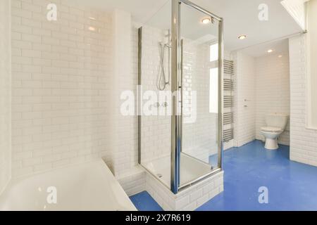 Ein gut beleuchtetes, elegantes Badezimmer mit glänzend weißen U-Bahn-Fliesen, einer großen Badewanne, einer Glasdusche und einem beheizten Handtuchhalter in Schapenbu Stockfoto