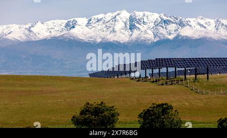 Solarenergiepark mit Reihen von Paneelen vor dem Hintergrund majestätischer schneebedeckter Berge und eines klaren blauen Himmels. Stockfoto