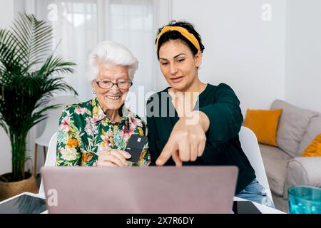 Eine junge Frau und eine ältere Dame sitzen mit einem Laptop an einem Tisch und nehmen einen Podcast auf, den die jüngere Frau auf den Bildschirm zeigt und den Sen führt Stockfoto