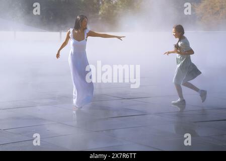 Frau, ihre Tochter, die Spaß im städtischen Dampfbrunnen hat Stockfoto