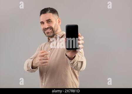 Lächelnder Bärenmann, der ein Smartphone vor grauem Hintergrund hält Stockfoto