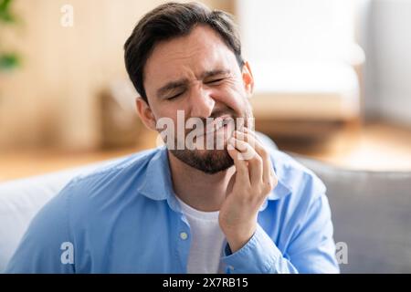 Bärtiger Mann, der mit Zahnschmerzen auf der Couch sitzt Stockfoto
