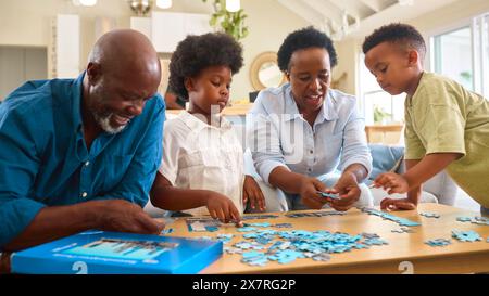 Großeltern Mit Enkelkindern Sitzen Zuhause Um Den Tisch Und Machen Gemeinsam Puzzle Stockfoto
