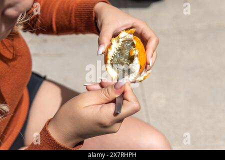 Nahaufnahme von Frauenhänden, die Nahrung von einer Passionsfrucht mit einem Löffel im Hof nehmen Stockfoto