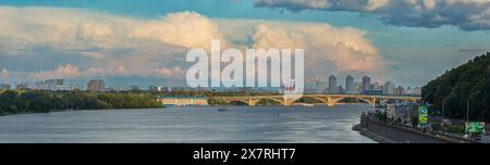 Die untergehende Sonne hebt die Kiewer U-Bahn-Brücke über den Fluss Dnieper mit malerischen Gewitterwolken am Himmel wunderschön hervor. Stockfoto