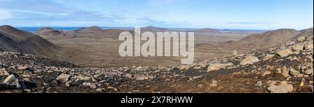 Karges Panorama der Halbinsel Reykjanes mit alten Lavafeldern, schmutziger gewundener Straße und vulkanischen Bergen im Hintergrund, blauer Himmel. Stockfoto