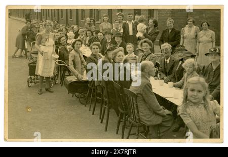 Originale, eindrucksvolle Postkarte aus dem 2. Weltkrieg mit der Feier zum Ende des 2. Weltkriegs/zur Feier der Friedensparty für VJ/Tag des Sieges in Japan. Hier sind Frauen und Kinder und ältere Männer, die draußen auf einem langen Tisch in ihrer städtischen Straße Tee trinken, viele Charaktere, ein freches junges Mädchen schaut in die Kamera. Eine lebendige Szene. Eine typische britische Straßenparty mit vielen Tassen Tee. Hauptsächlich Party für ältere Frauen und ein paar Männer. Vintage Devon. Foto vom August 1945, Salisbury Street, Exmouth, Devon, England, GROSSBRITANNIEN Stockfoto