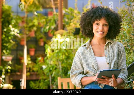 Porträt Einer Lächelnden Jungen Erwachsenen Frau Mit Digitalem Tablet, Das Im Gartenzentrum Arbeitet Und Pflanzen Überprüft Stockfoto
