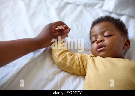 Nahaufnahme der liebevollen Mutter, die die Hand des Babys hält, während sie zu Hause auf dem Bett schläft Stockfoto