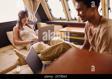Ein multikulturelles Paar entspannt sich auf einem Sofa mit einem Laptop, um Online-Aktivitäten zu betreiben. Stockfoto
