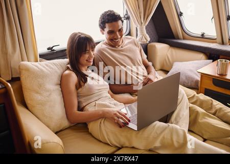 Ein Mann und eine Frau verschiedener Ethnien sitzen auf einer Couch, vertieft darin, zusammen einen Laptop zu benutzen. Stockfoto