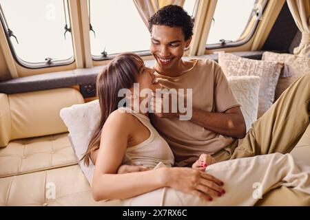 Ein interrassisches Paar sitzt bequem auf einer Couch und genießt die Gesellschaft der anderen in einer gemütlichen Umgebung. Stockfoto