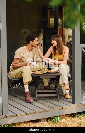 Ein Paar zwischen Rassen genießt ein köstliches Essen zusammen an einem Tisch draußen, umgeben von Natur und der warmen Umarmung der Liebe. Stockfoto
