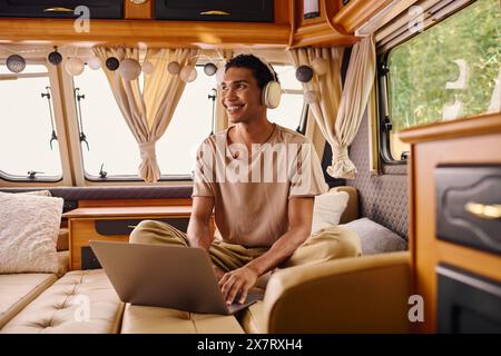 Ein Mann mit vielseitiger Abstammung sitzt bequem auf einem Sofa, vertieft in seinen Laptop-Bildschirm und konzentriert sich vollständig auf seine digitale Welt. Stockfoto