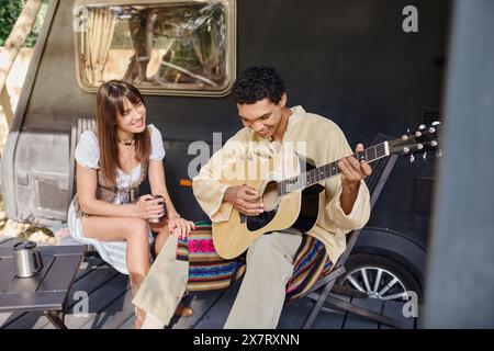 Ein Mann, der neben einer Frau eine Gitarre spielt, in einer romantischen Umgebung, umgeben von der Natur, und sich gegenseitig in Gesellschaft genießt. Stockfoto