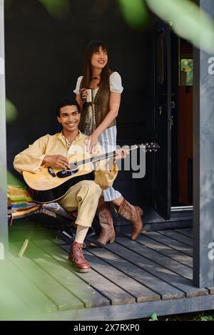 Ein Mann und eine Frau sitzen auf einer Veranda, spielen eine Gitarre und genießen sich in einer ruhigen Umgebung. Stockfoto