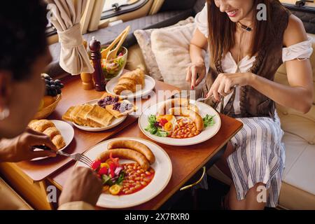 Eine Frau sitzt an einem Tisch und genießt während eines romantischen Kurzurlaubs in einem Wohnmobil eine Vielzahl köstlicher Gerichte. Stockfoto