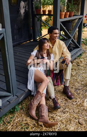 Ein Mann und eine Frau verschiedener Rassen entspannen sich gemeinsam auf einer hölzernen Veranda und genießen einander Gesellschaft in einer friedlichen Umgebung. Stockfoto