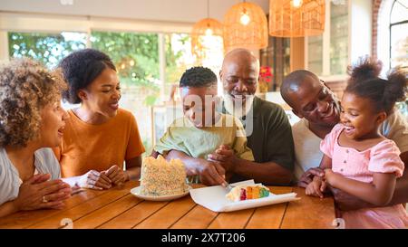 Mehrgenerationsfamilie feiert zu Hause den Geburtstag des Enkelsohnes und bläst Kerzen auf Kuchen aus Stockfoto