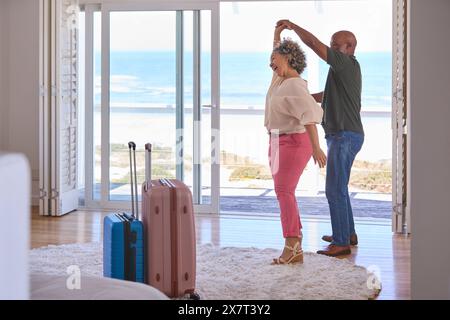 Älteres Paar Mit Gepäcktanz Im Beachfront House Mit Blick Auf Den Ozean Für Sommerurlaub Stockfoto