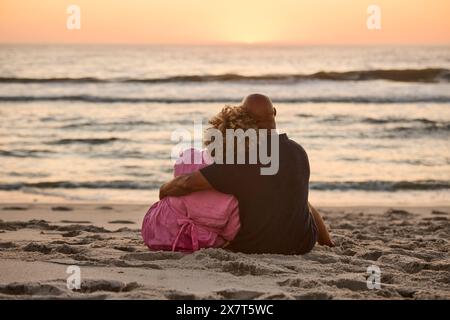 Rückansicht Des Älteren Ehepaares, Das Am Strand Sitzt Und Bei Sonnenuntergang Auf Das Meer Blickt Stockfoto