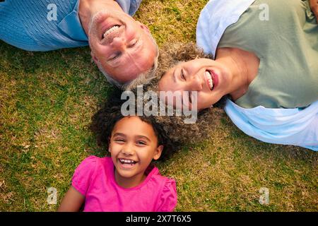 Auf Multi Racial Großeltern Mit Enkelin, Die Draußen Auf Gras Liegt Stockfoto
