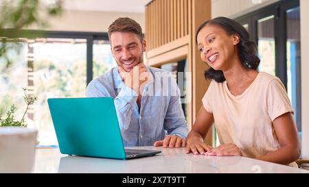 Lächelndes Multi-Racial-Paar Zu Hause, Das Zusammen Auf Laptop Schaut Stockfoto