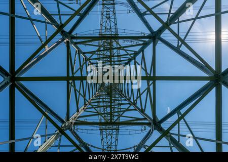 Ein großer Turm mit symmetrischer Struktur, mehreren Stromleitungen und einem blauen Himmel im Hintergrund. Das Design des Turms ist optisch Stockfoto