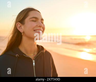 Lässig Gekleidete Junge Frau Mit Geschlossenen Augen Am Strand Mit Wunderschönem Sonnenaufgang Über Meer Stockfoto
